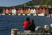 Couple assis sur le quai de Strandsiden admirant la vue sur le vieux port et les maisons de Bryggen de l'autre côté de la baie de Bergen.