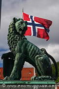 Drapeau norvégien flottant derrière la statue d'un lion de bronze qui orne le port de Bergen